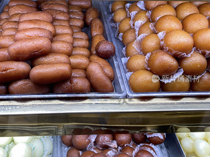 印度糖果店陈列的rasgulla和Gulab jamun(玫瑰水莓)Mithai(糖果)托盘的特写图像，重点放在前景